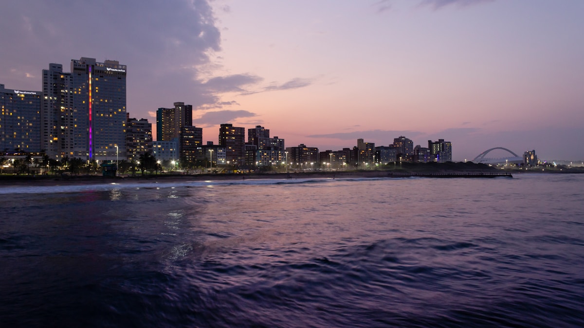 Aerial view of Durban's Golden Mile beachfront with breaking waves, lifeguard flags, and the city skyline behind